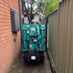 Maeda 285 mini crawler crane navigating a very narrow side access beside a house to access a tight‑access lift.