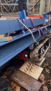 Tracked Carrier Hire - Tracked carrier transporting five steel beams through a narrow gateway on uneven ground
