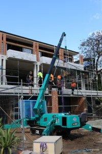 Maeda 305 mini crane lifting a large glass panel on a tight-access Tennyson Point construction site