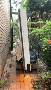 Tracked carrier transporting glass panel down a 900mm side path of a house in Turramurra