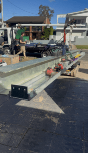 Tracked carrier transporting heavy steel beams through a garage and into the back of a property