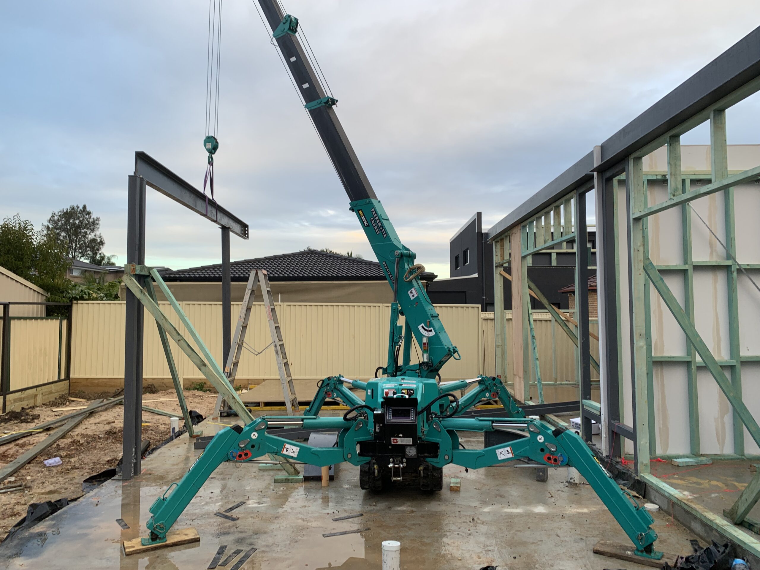 Maeda 285 mini crane installing structural steel in a tight-access backyard at a residential property.