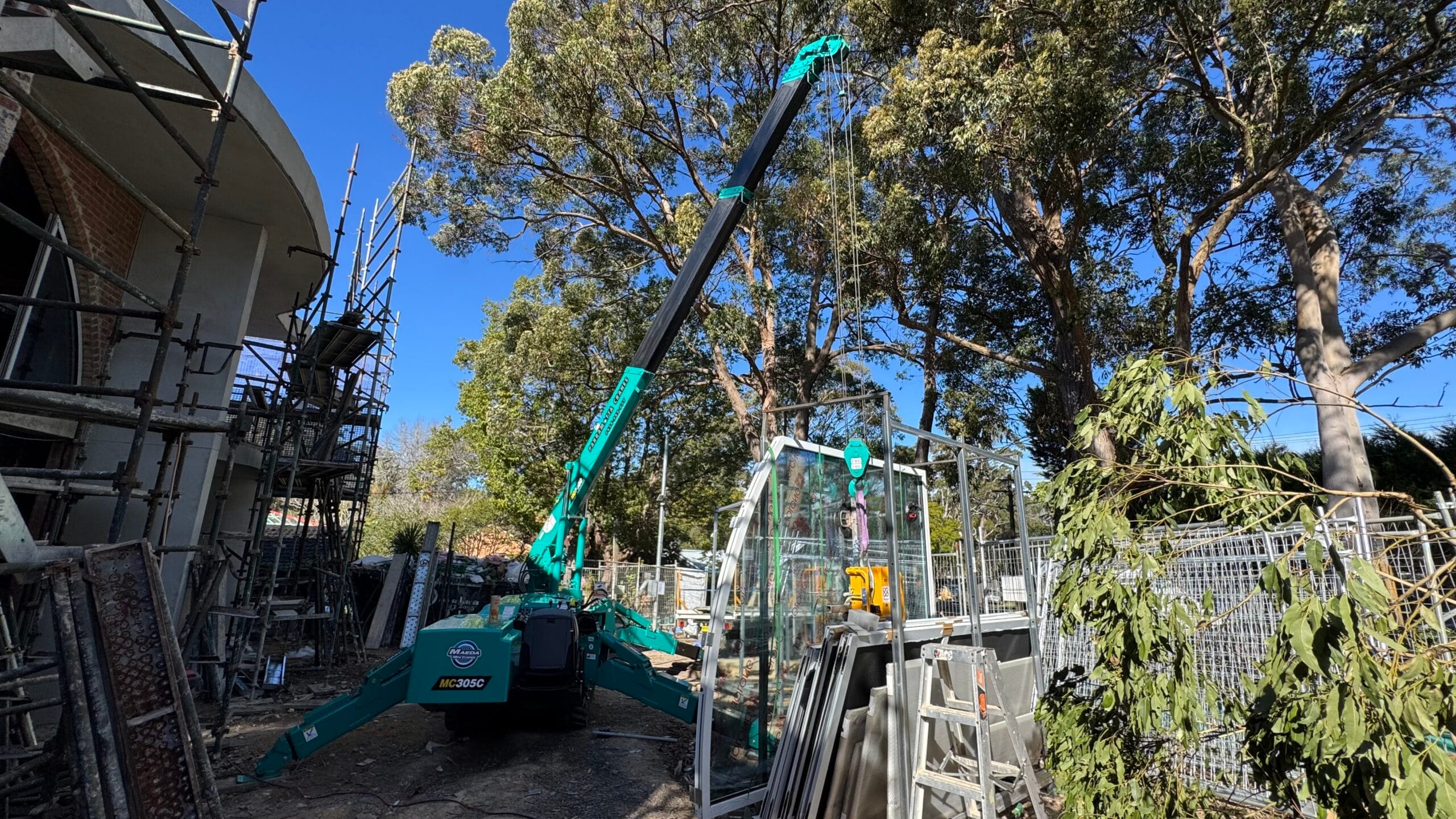Maeda MC305 mini crane using a glass lifter to install glazing under trees in Pymble with restricted overhead access.